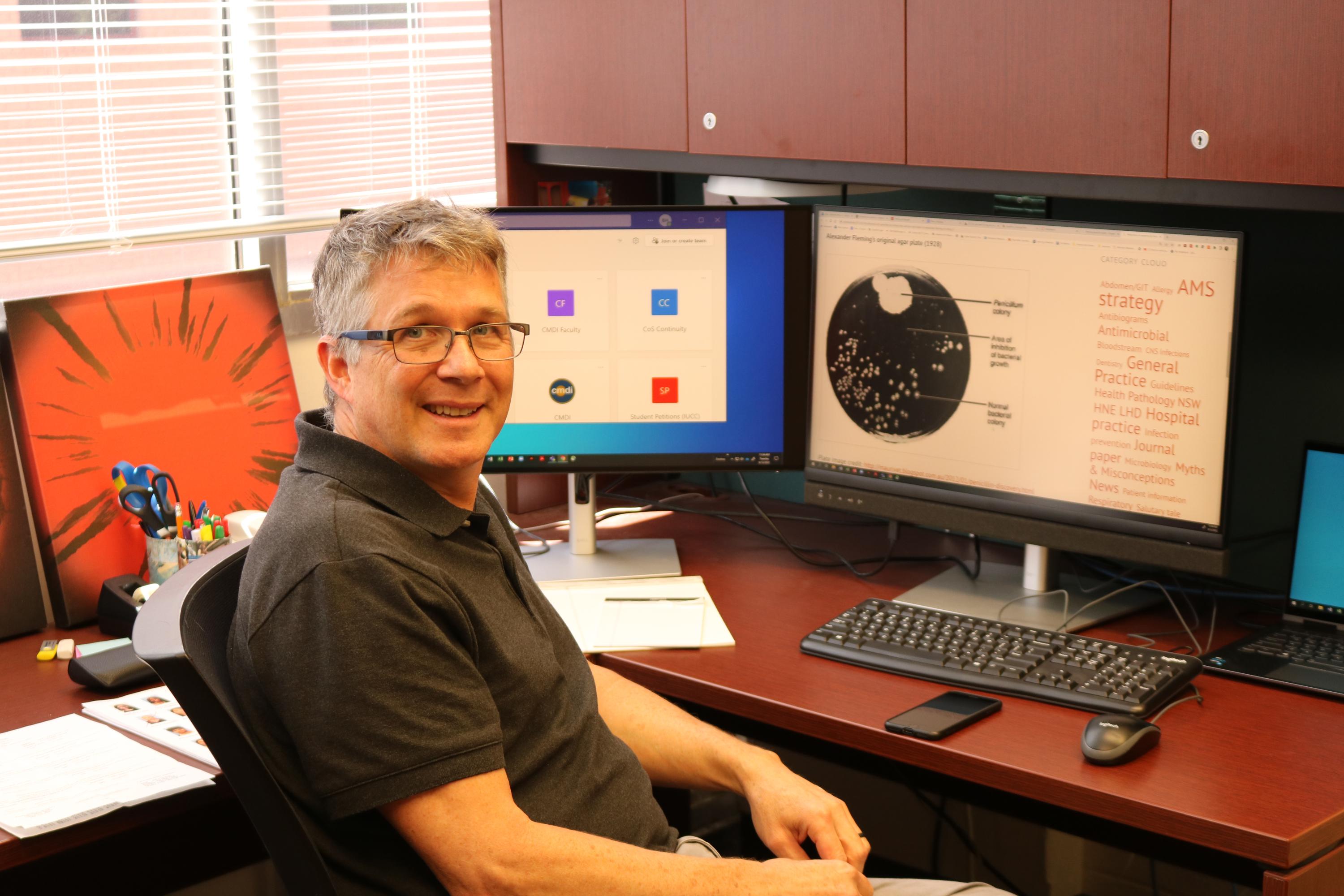 Brian Hammer in his office with an image from Alexander Fleming's original 1928 penicillin agar plate. (Photo Renay San Miguel)